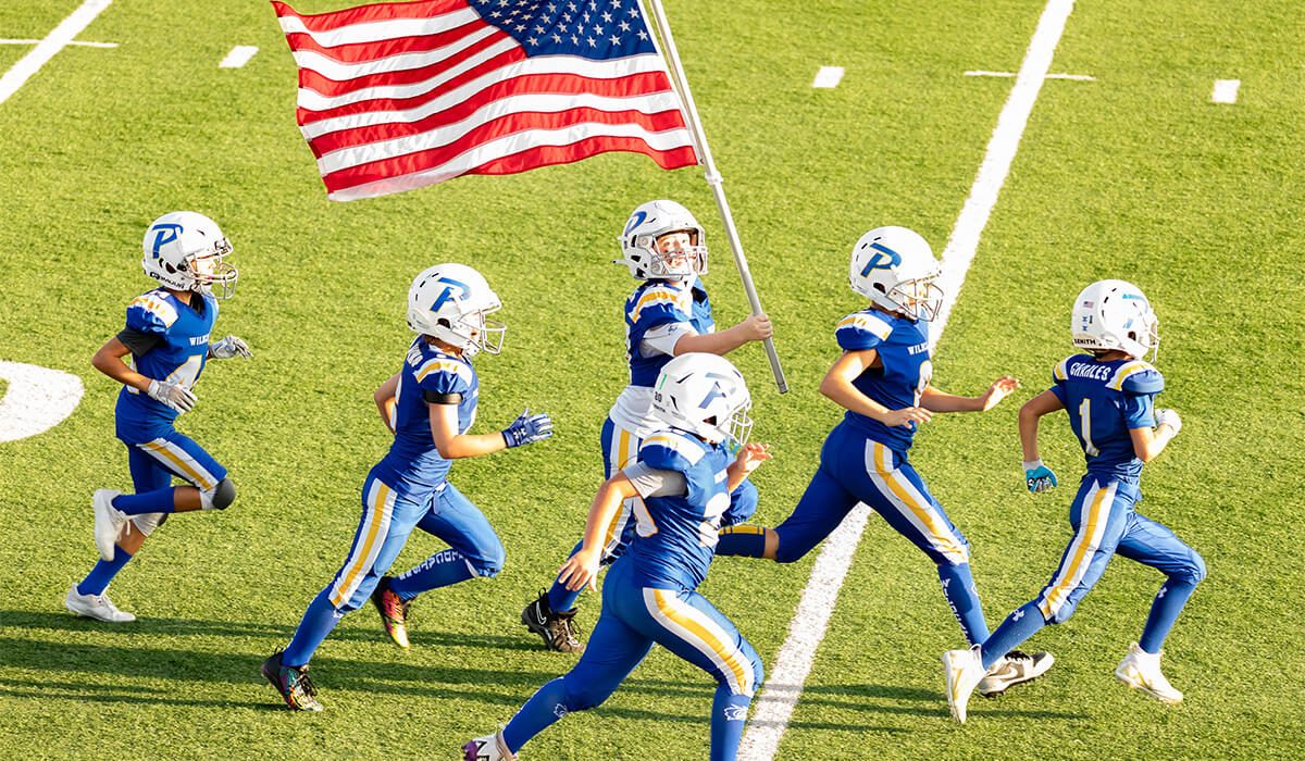 The Piedmont Youth Football players running onto the field with the American flag. 